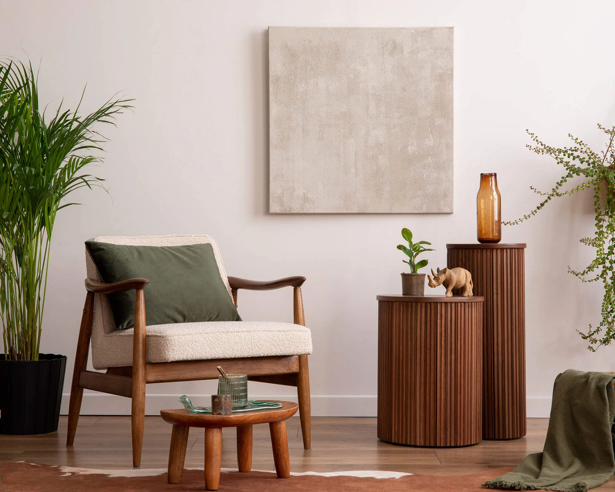 Stylish Living Room with Modern Furniture and Greenery A cozy living room featuring a wooden armchair, decorative tables, and indoor plants, complemented by a neutral artwork on the wall.