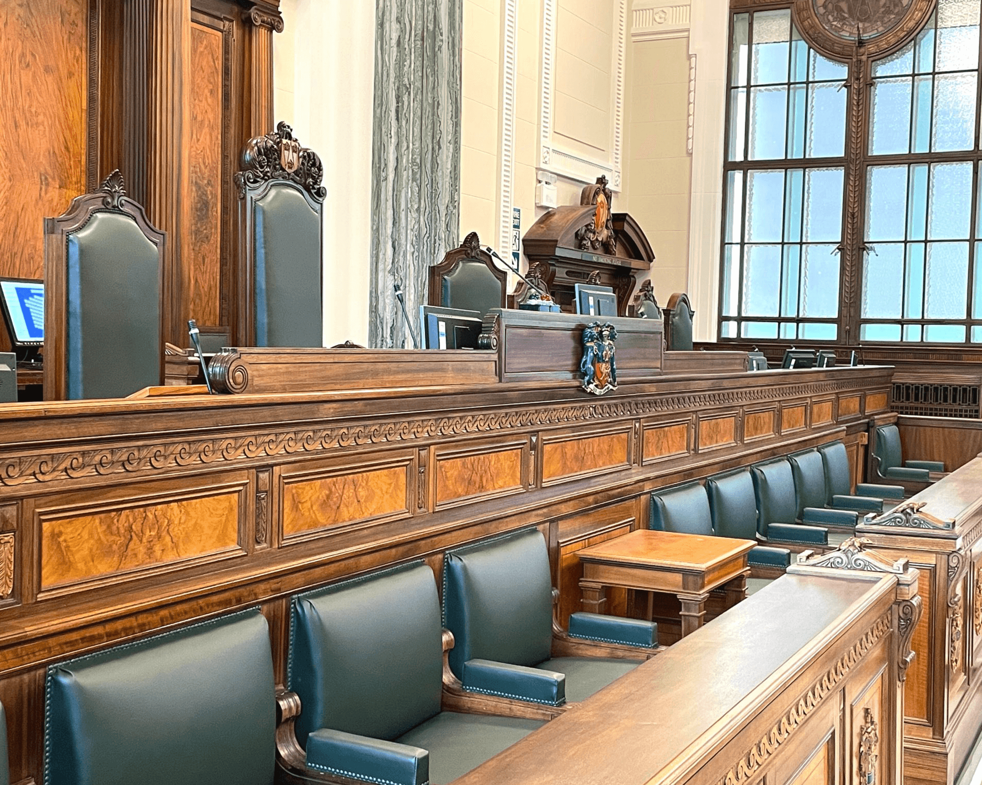 View of a traditional courtroom featuring wooden benches, green upholstered seats, and decorative architecture.