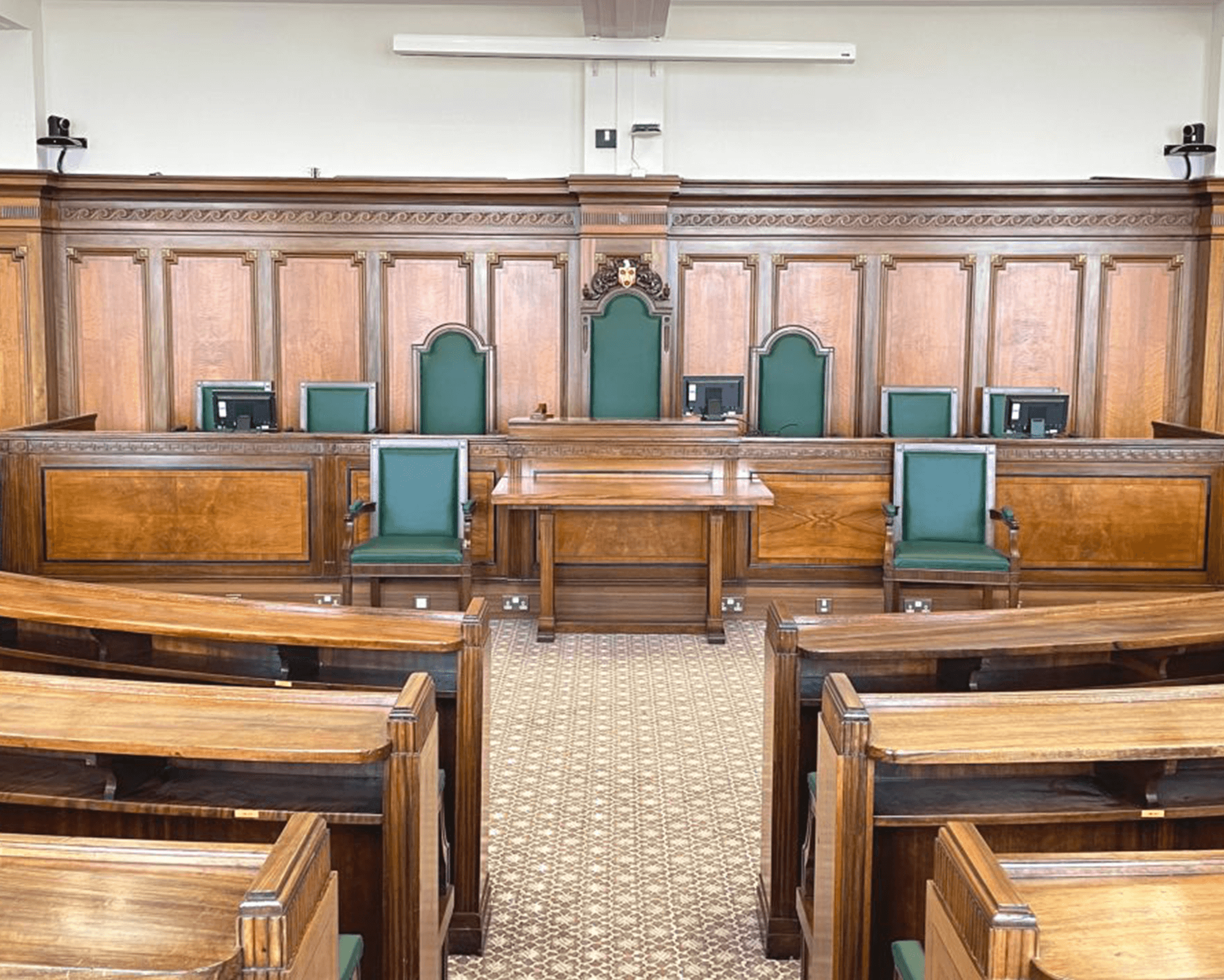 Interior view of a courtroom featuring wooden paneling and green seating, showcasing judge's bench and juror chairs.