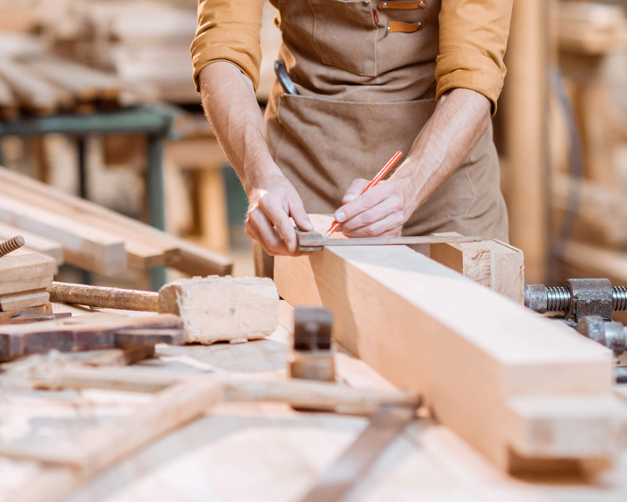 A carpenter carefully measuring a piece of wood with a pencil in a woodworking shop, surrounded by various tools and materials.