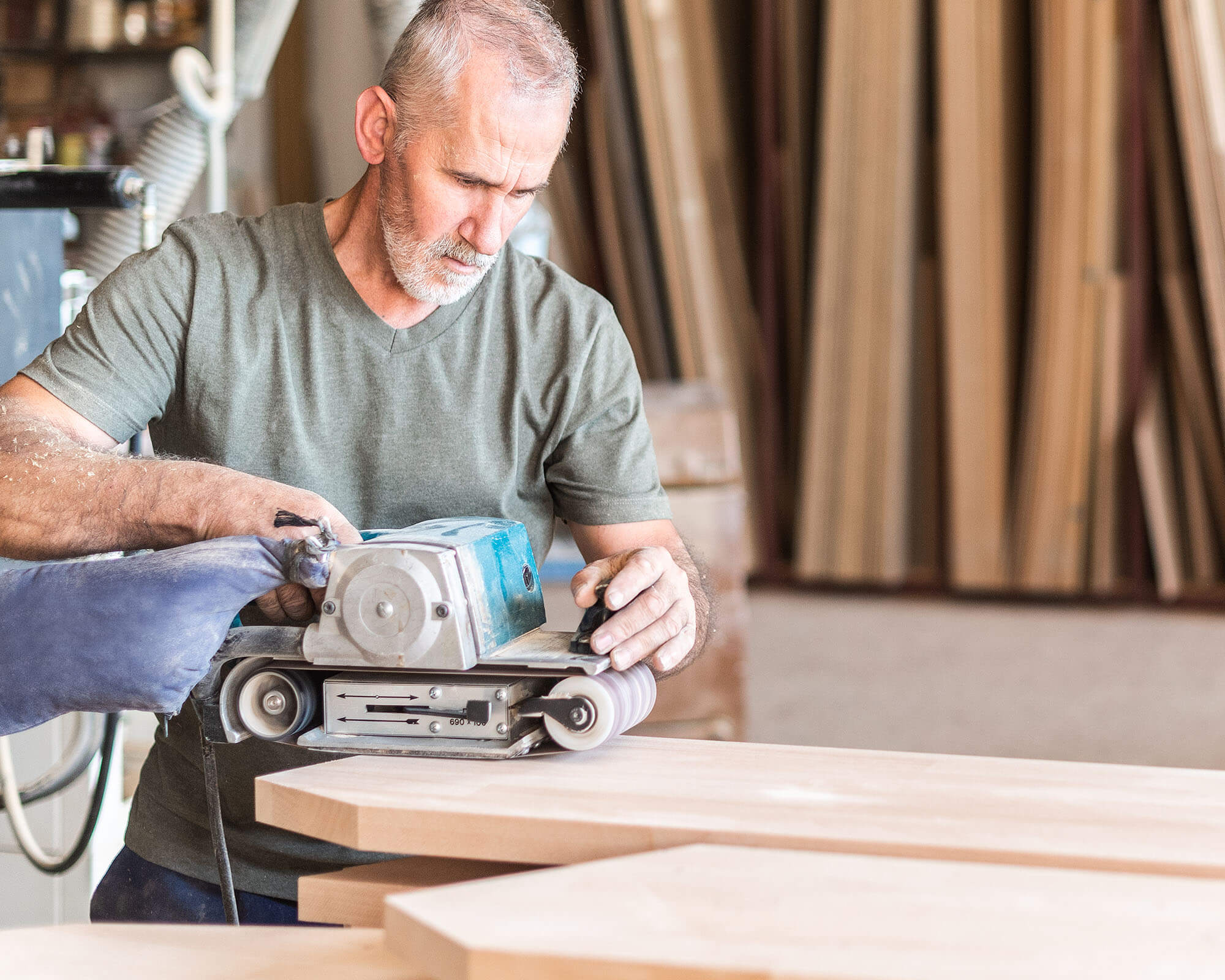 A man working with a power sander on wooden boards in a woodworking shop.