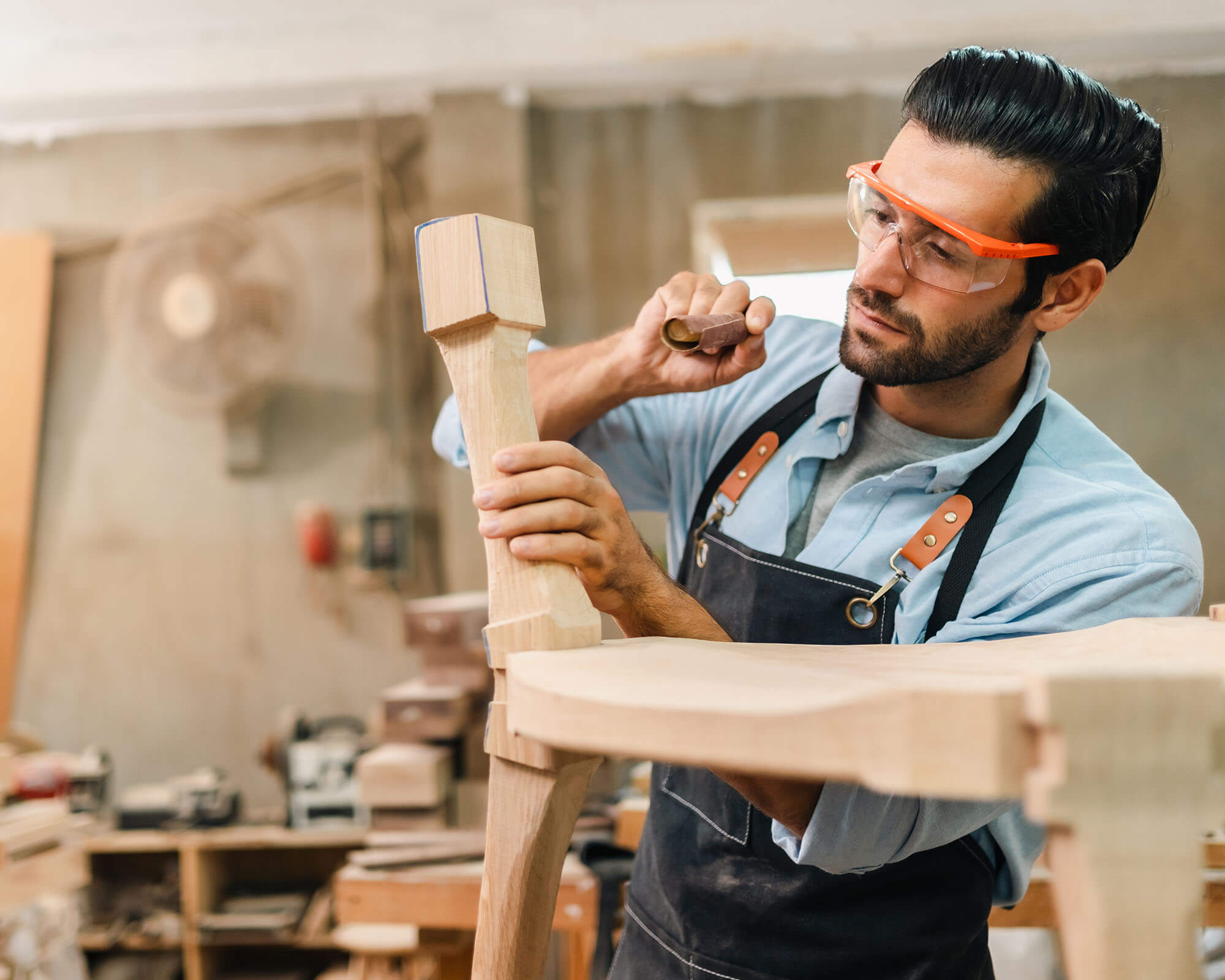 A skilled woodworker carefully carving a wooden piece with a chisel in a well-equipped workshop.
