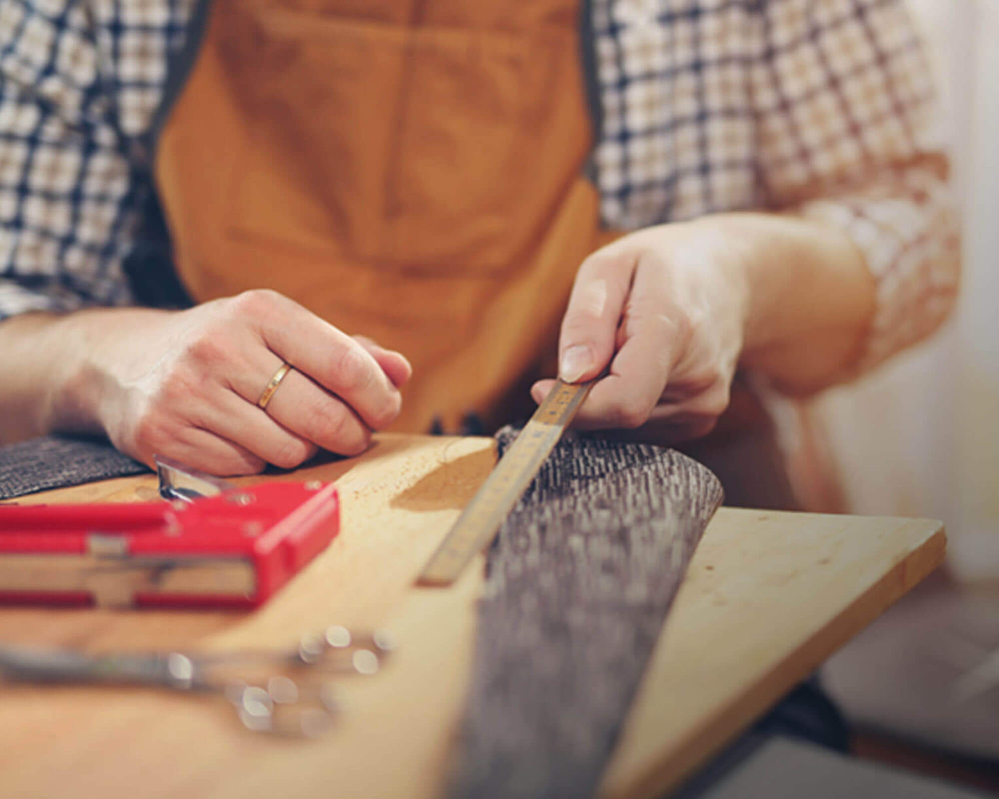Close-up of a person's hands measuring fabric with a ruler in a workshop, surrounded by crafting tools.