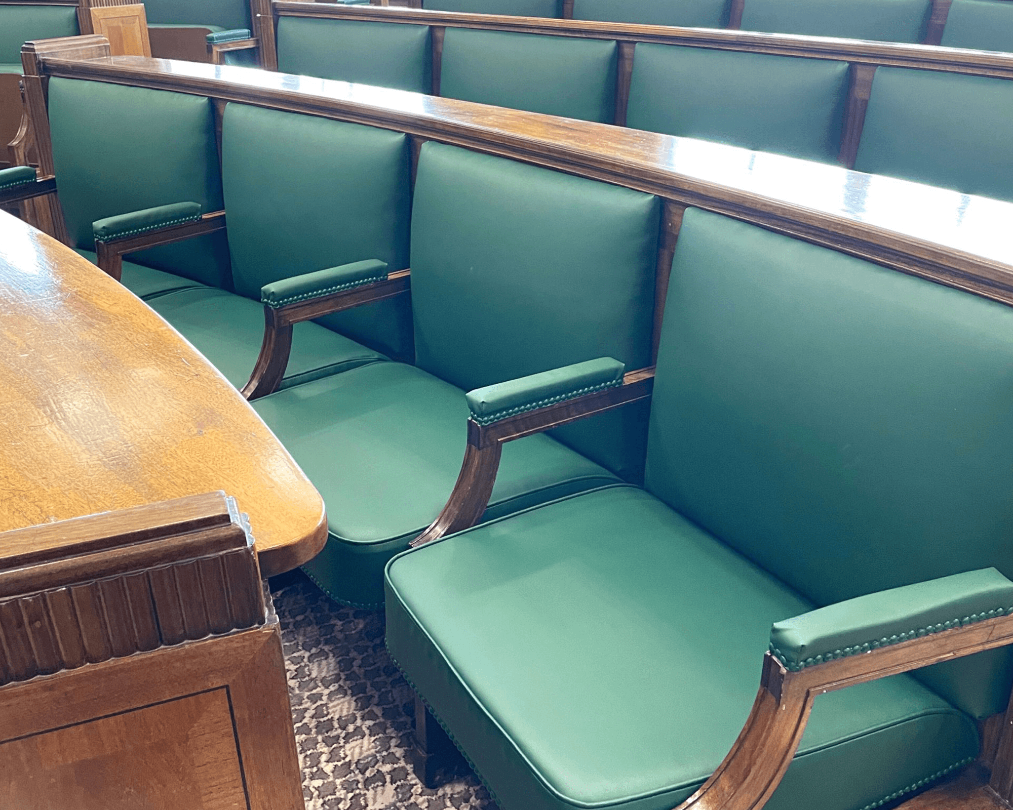 Interior view of a meeting room featuring green upholstered seats and a wooden table.