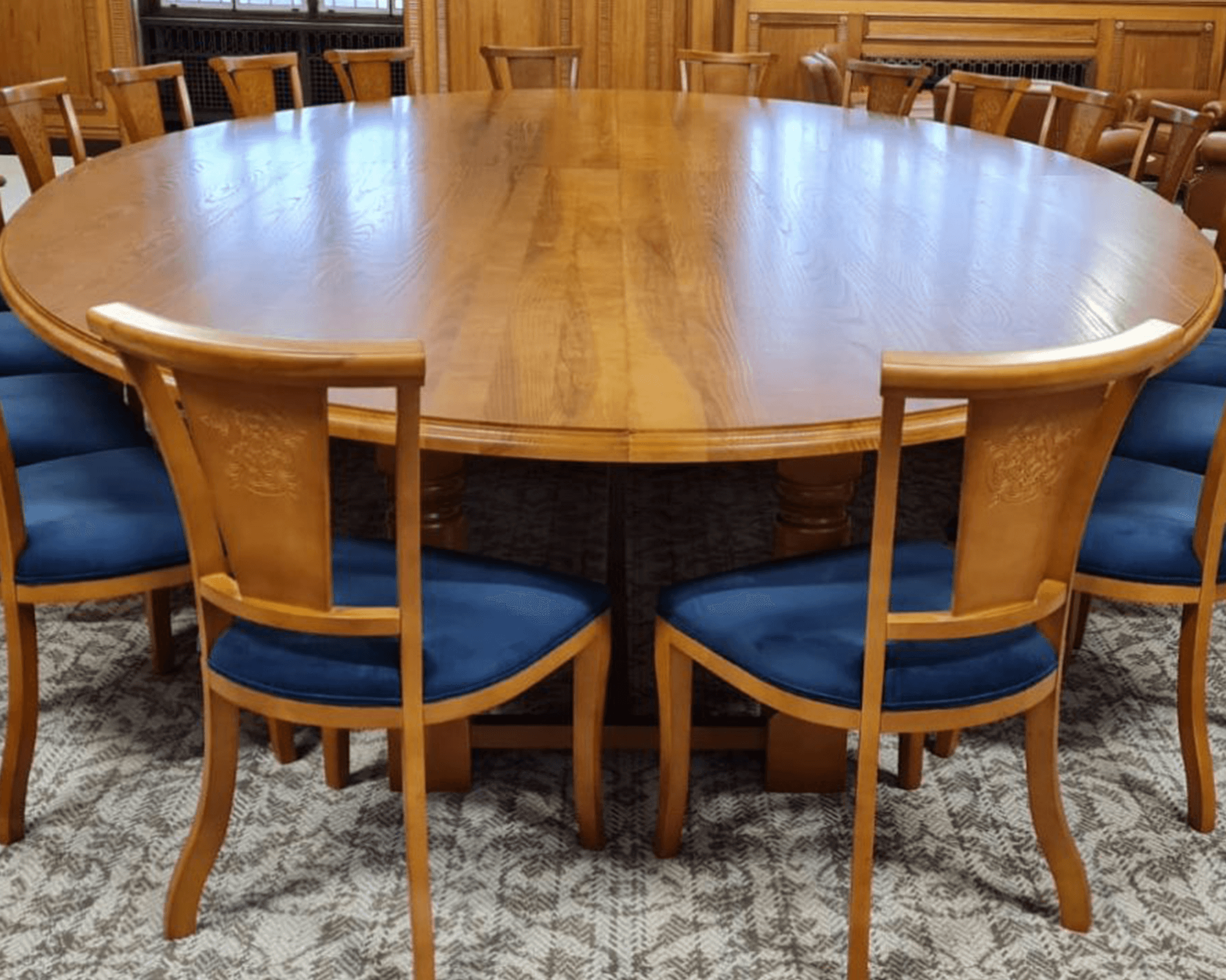 A large round wooden conference table surrounded by blue upholstered chairs in a formal setting.